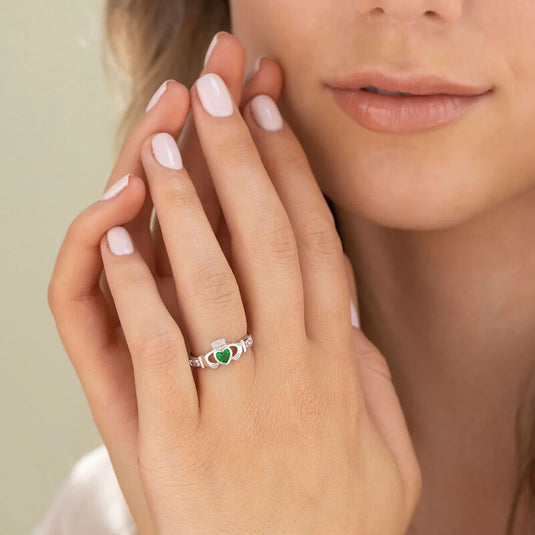 Close-up of a hand wearing a sterling silver Claddagh ring with a green synthetic emerald heart centerpiece.