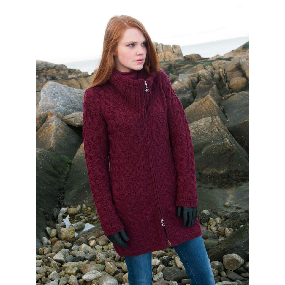 Woman wearing a long burgundy knitted coat standing on rocky shore