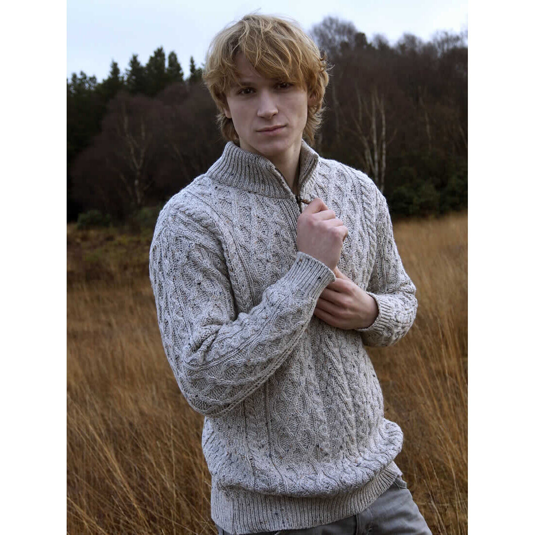 Male model wearing an oatmeal cable knit Aran half zip sweater in a field with tall grass